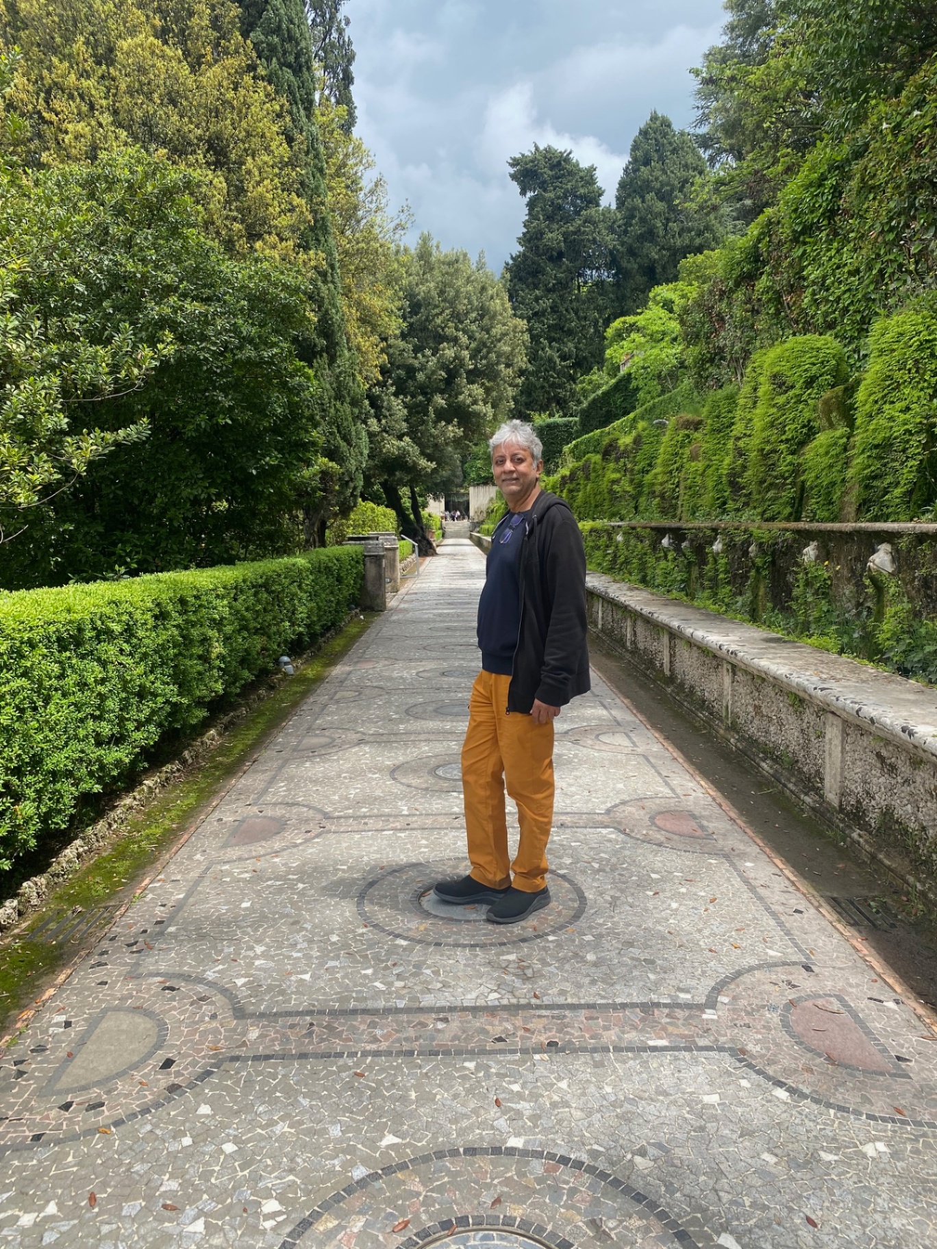 Roberto at an Italian villa garden path framed by cypress and hedges.