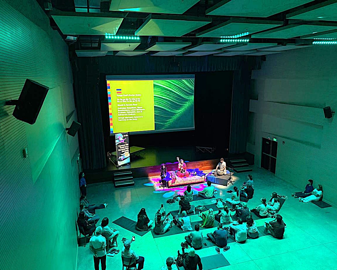 Wide view of the ensemble performing to a seated audience under green stage lights.
